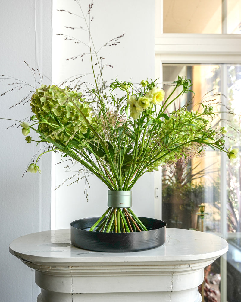 Bouquet professionnel avec un beau volume en torsade de fleurs Hanataba Matcha Green, présenté sur un plateau floral noir au sommet d'un piédestal blanc.