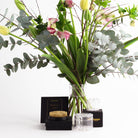 Le kit de création florale Hanataba est présenté avec une torsade de bouquet en cristal transparent contenant des tiges d'eucalyptus, des fleurs roses et des boutons verts, à côté d'une grenouille à épingles à fleurs. L'élégant emballage noir met en valeur le logo doré d'Hanataba. Le tout sur un fond blanc épuré.