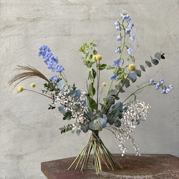 Arrangement floral Ikebana composé de delphiniums bleus, de craspedia jaunes et de délicate haleine de bébé, arrangés à l'aide d'un porte-tige traditionnel Hanataba à spirale selon les techniques japonaises.