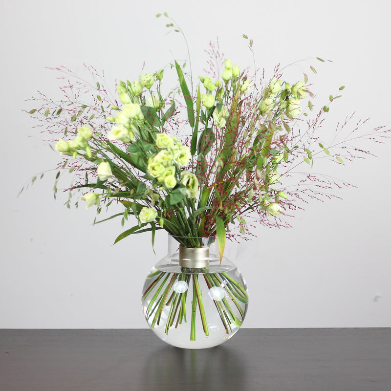 Une présentation florale de style Ikebana avec des fleurs vertes fraîches et des accents roses délicats, arrangés avec art et soutenus par un support de tiges en spirale Hanataba.