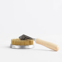 A comb-like kenzan rake, cleaning tool,  with a wooden handle on top of a flower frog,  on a white background.