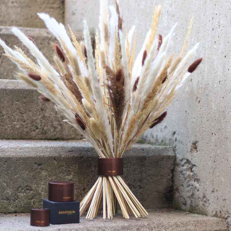 Un vire-bouquet Hanataba de Muddy Brown soutient élégamment un arrangement d'herbes et de roseaux séchés sur des marches en béton, accompagné de deux récipients Hanataba assortis.