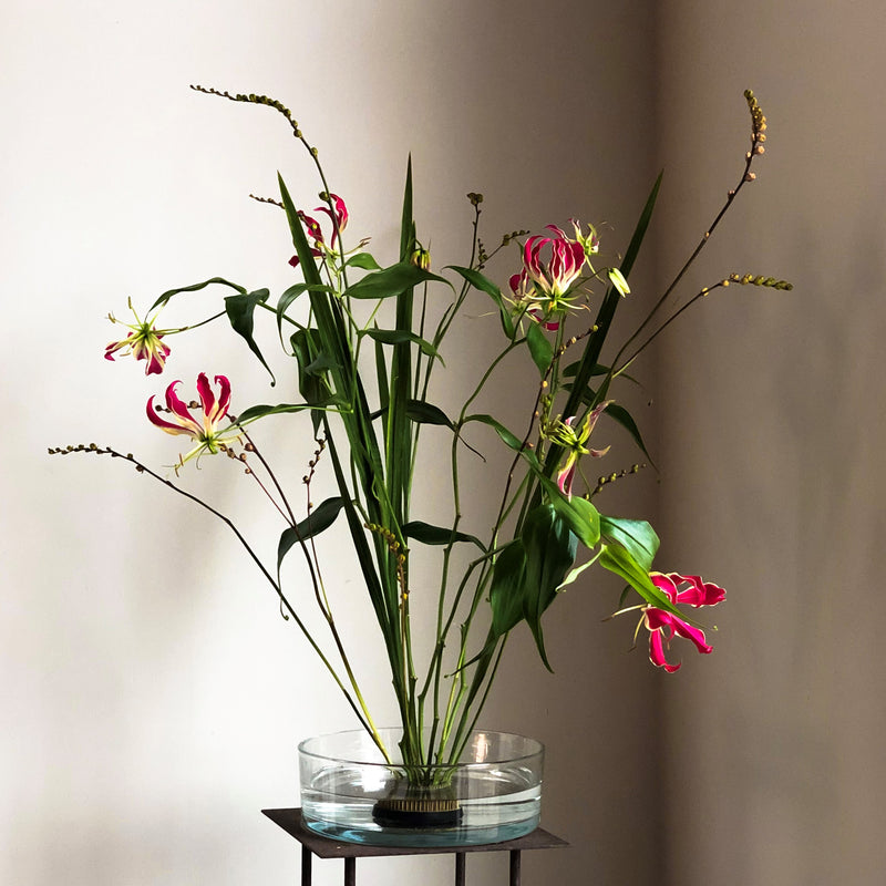 Lys gloriosa exotiques aux pétales roses et jaunes frappants, ancrés par un anneau Kenzan de 70 mm dans une coupelle en verre.