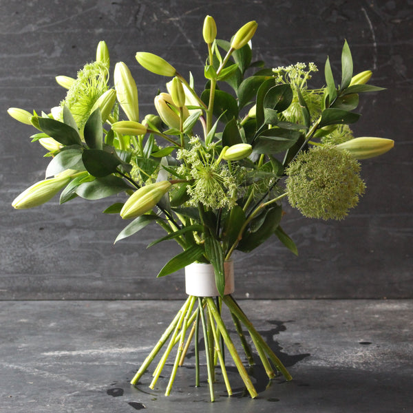 Bouquet de fleurs fraîches vertes et blanches serré par un twister Hanataba Pearly Silver sur un fond sombre.