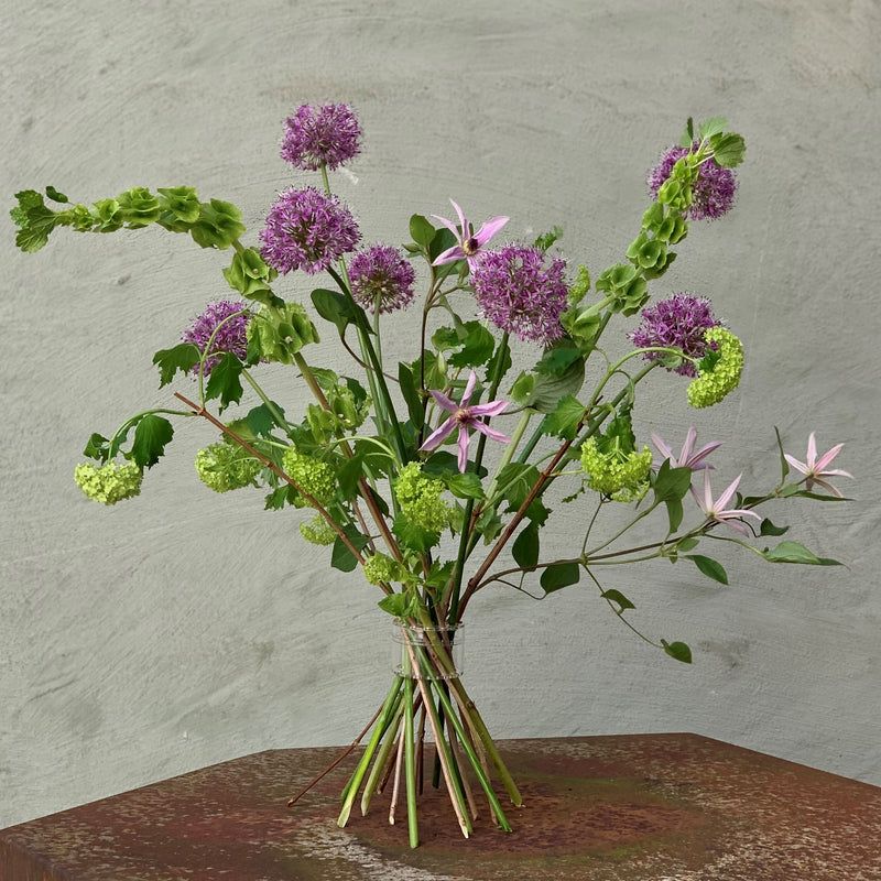 Une tordeuse de bouquet Hanataba permet de fixer un ensemble vibrant d'alliums violets et de fleurs roses délicates sur une toile de fond murale discrète.