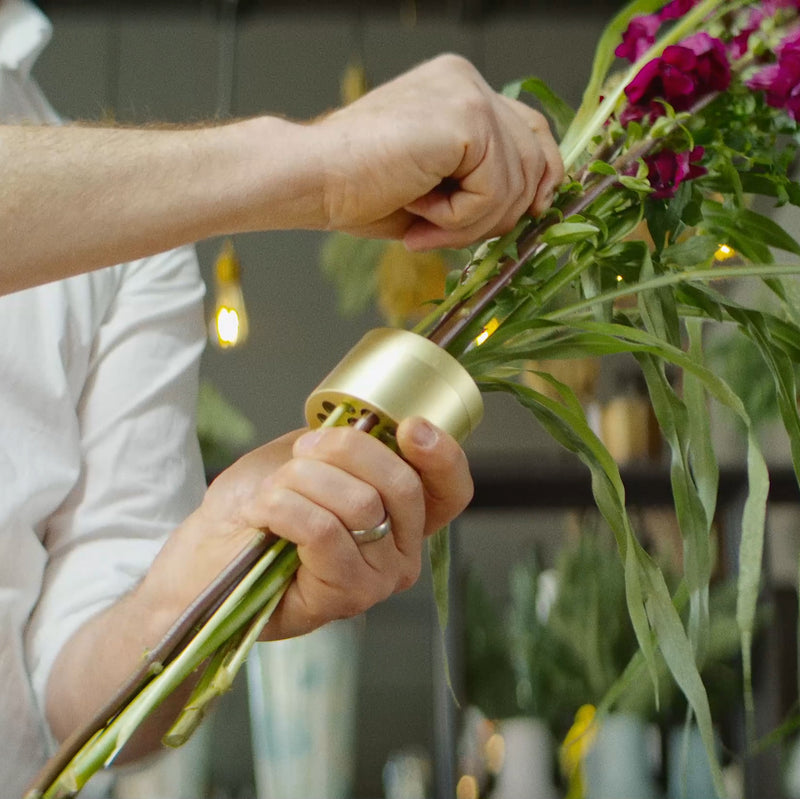 Les mains d'un homme montent habilement une composition florale vibrante à l'aide d'un Hanataba Champagne Gold.