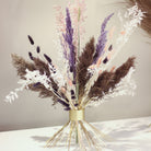 Un bouquet Hanataba Champagne Gold avec un feuillage violet, noir et blanc sur un fond neutre, mettant en valeur l'élégance moderne.