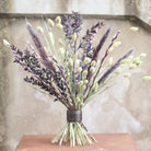 Un bouquet de feuillage violet foncé et de fleurs vert clair fixé à l'aide d'un twister Hanataba Pitch Black sur une surface en bois.