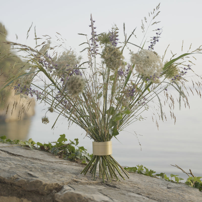 Des fleurs sauvages, dont des épis violets et des grappes blanches, ont été rassemblées dans un bouquet torsadé Hanataba or champagne sur une corniche rocheuse surplombant des eaux calmes.